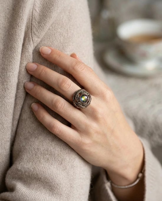 Verstelbare koperen ring met Mystic Topaz in een koepelvormig ontwerp, gedragen op de vinger bij een beige trui.