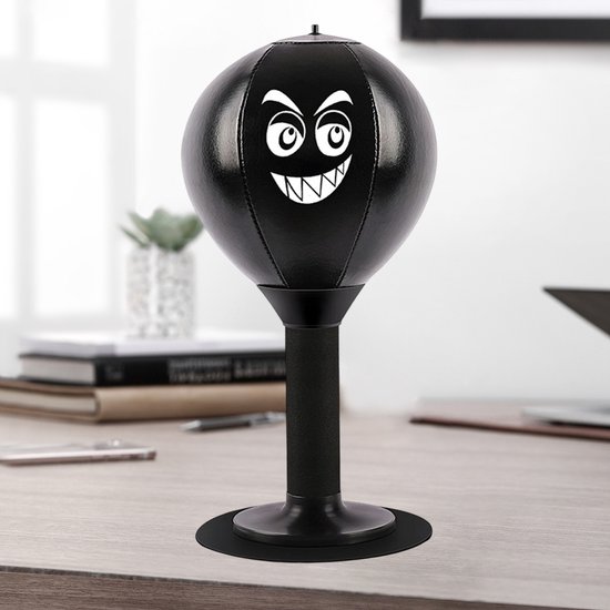 Zwarte desktop bokstrainer met boze gezicht, op een bureau naast een laptop en plant.