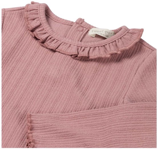 Detailopname van een roze baby shirt met ruches bij de kraag en label met tekst Sweet Petit.