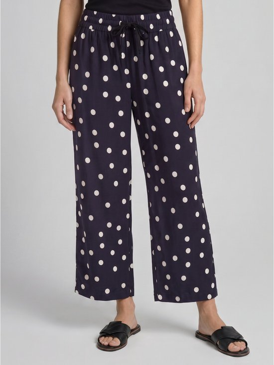 Onderlichaam van een model in een marineblauwe culotte met witte polkadotprint, wijde pijpen en strikceintuur.