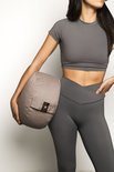 Vrouw in grijze sportkleding houdt een rond, taupe meditatiekussen vast met een loglabel.