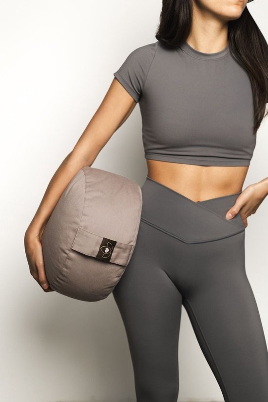 Vrouw in grijze sportkleding houdt een rond, taupe meditatiekussen vast met een loglabel.