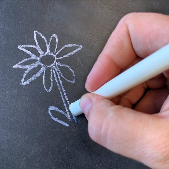 Hand tekent een bloem met witte krijt op een zwart schoolbord.