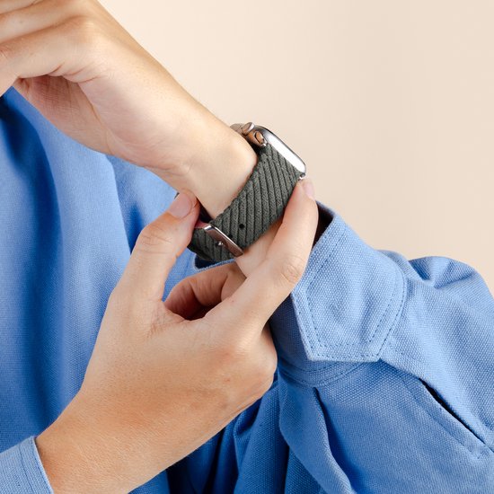 Iemand bevestigt een groen, corduroy horlogebandje met gesp aan een smartwatch om de pols.