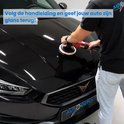 Man polijst de glanzende motorkap van een zwarte auto met een rode polijstmachine en witte polijstpad.