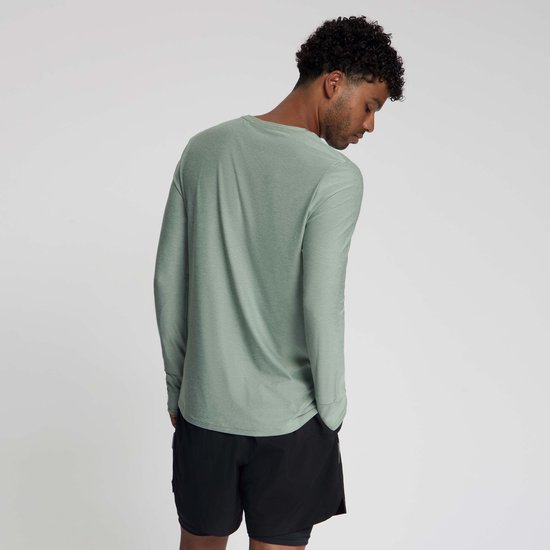 Man met gekruiste armen draagt een groen Rogelli hardloopshirt met lange mouwen en zwart sportbroekje, kijkt naar beneden.