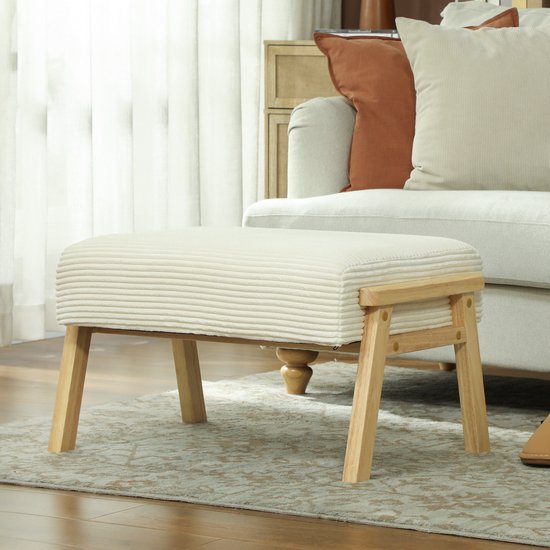 Crèmewit voetenbankje met corduroy bekleding en houten frame, naast een bank.