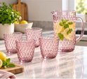 Carafe rose en verre remplie d'eau, de citron et de menthe, à côté de verres roses à motif nid d'abeille.