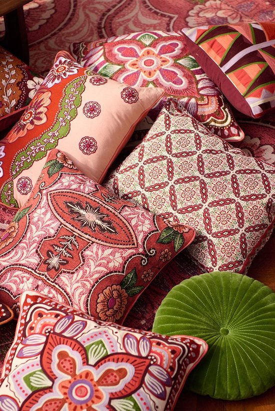 Een stapel rood/roze sierkussens met diverse bloemen- en paisleyprints in oranje, groen en paars. Een groen, rond kussen ligt rechtsonder.