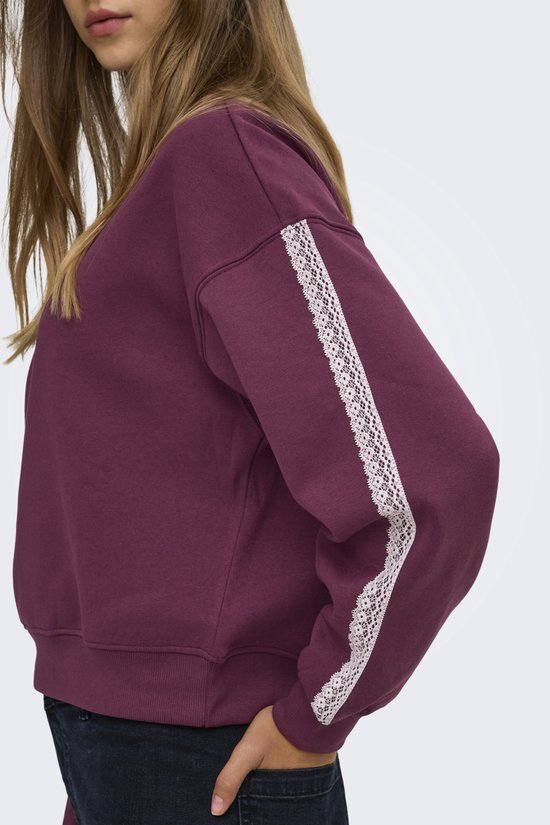 Zijaanzicht van een model in een paarse sweater met een witte kanten strook langs de mouw.