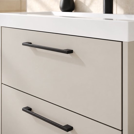 Detailopname van beige lades met strakke, zwarte handgrepen en een witte wastafelrand.