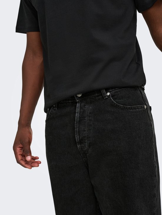 Detailopname van een zwarte spijkerbroek met losse pasvorm gedragen onder een zwart T-shirt.