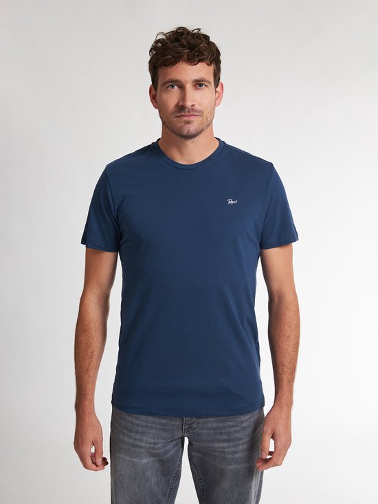 Model draagt een donkerblauw T-shirt met Petrol-logo op de borst, gecombineerd met een grijze spijkerbroek.