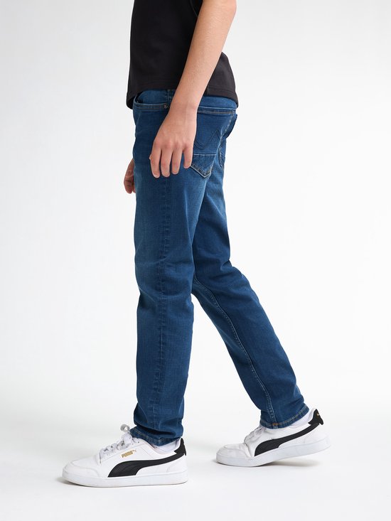 Zijaanzicht van Petrol Industries regular tapered stretch jeans in blauw, gecombineerd met witte Puma sneakers.