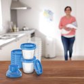Stapel Philips Avent bewaarbekers met blauwe deksels, voor babyvoeding. Op de achtergrond een vrouw met baby in keuken.