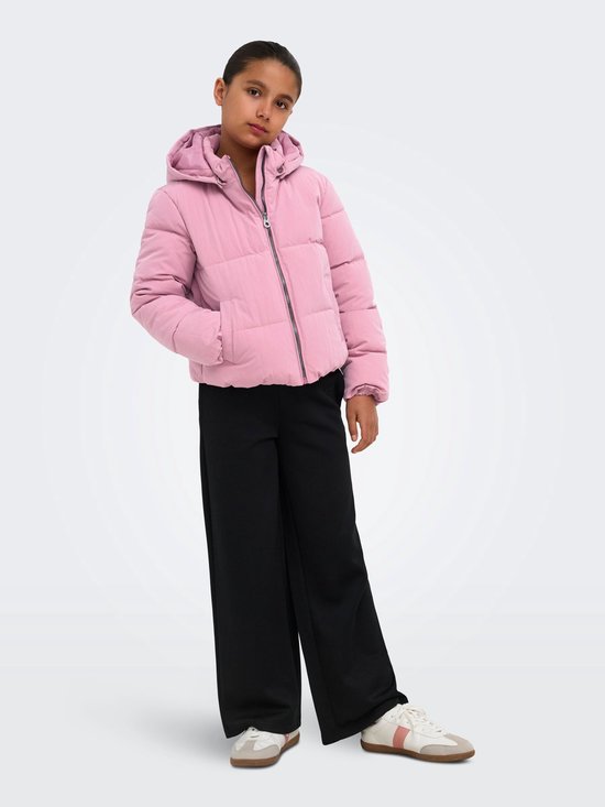 Meisje met een roze pufferjack met capuchon, zwart broek, witte sneakers.