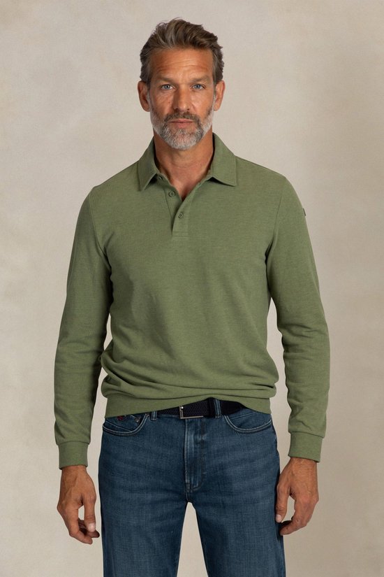 Man met grijze baard, die een lichtgroen poloshirt met lange mouwen en donkerblauwe jeans draagt.
