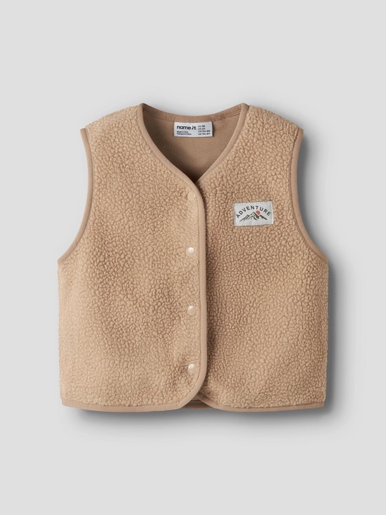 Beige teddy gilet met drukknoopsluiting en een 'Adventure' patch op de borst. Model van voren.