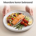 Een witte bord met zalm, asperges, tomaten, citroen en salade, vastgehouden door twee handen.