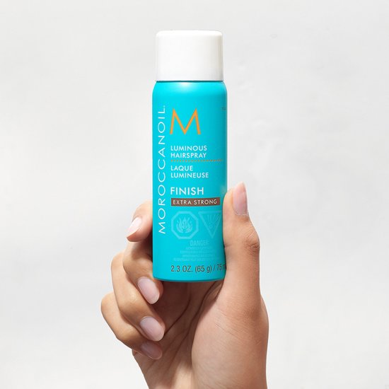 Hand met turquoise Moroccanoil Luminous Hairspray Extra Strong fles, 2.3 oz.