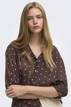 Close-up van een model met een bruine blouse met witte stippen.