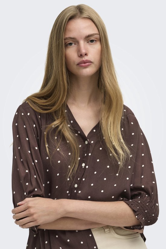 Close-up van een model met een bruine blouse met witte stippen.