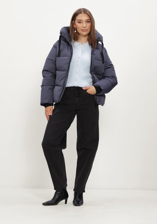 Model in een donkerblauwe, korte, gepofte jas met capuchon, lichtblauwe cardigan en zwarte jeans.