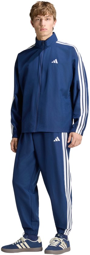 Man in een donkerblauw trainingspak met witte strepen en Adidas logo's.