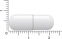 Eén witte capsule naast een liniaal met millimeters en centimeters.
