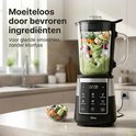 Zwarte en zilveren blender met groene smoothie en bevroren groenten in de kan.