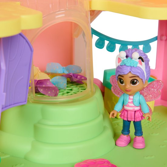 Gabby pop met blauwe jas, roze rok en paarse haren naast een roze huisje met vlinderdetails.
