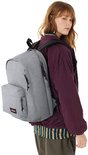 Vrouw met een grijze Eastpak rugzak op haar rug, met een bordeaux jasje en gestreept shirt.