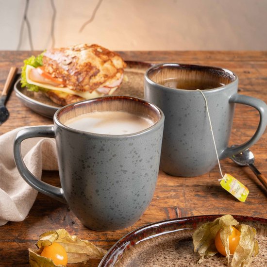 Twee grijze mokken met bruine binnenkant op een houten tafel. Eén mok met koffie, de ander met thee.