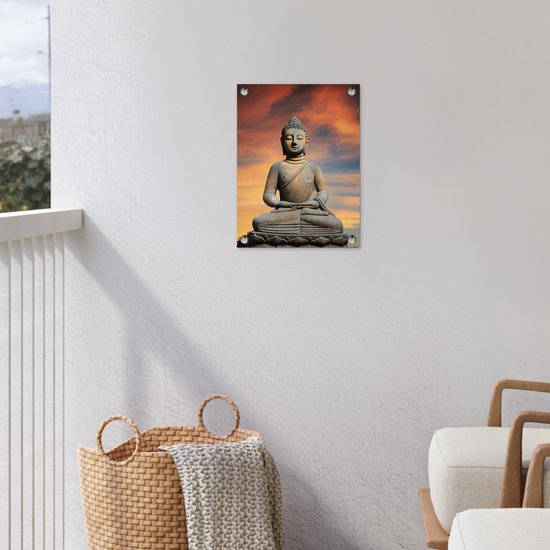 Bouddha en pierre sur fleur de lotus sur fond de coucher de soleil orange, suspendu à un mur blanc avec un panier.