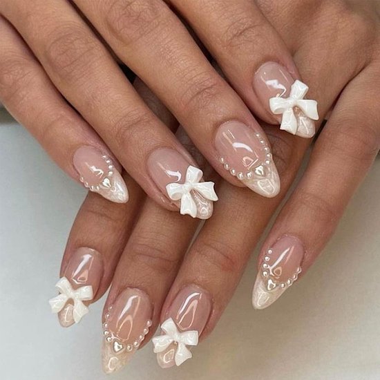 Mains avec ongles amande: base nude, bouts français blancs, perles et nœuds.
