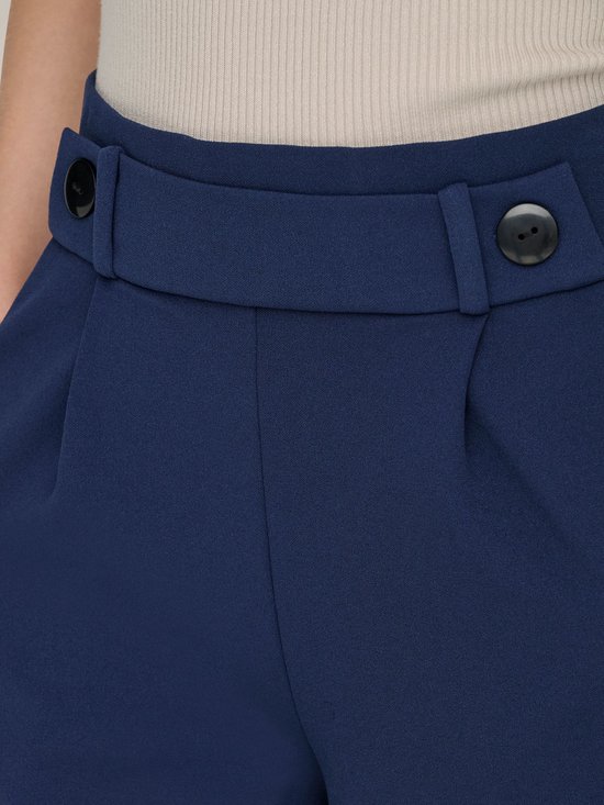 Sluiting van marineblauwe wijde broek met twee knopen en een stoffen riem.