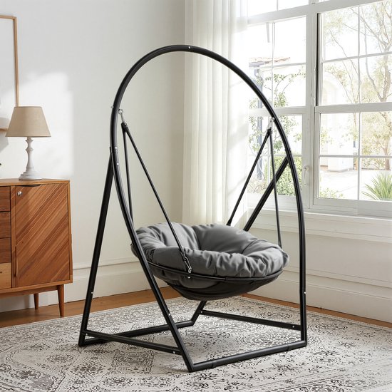 Grijze hangstoel met een rond zwart metalen frame, geplaatst op een vloerkleed in een woonkamer.