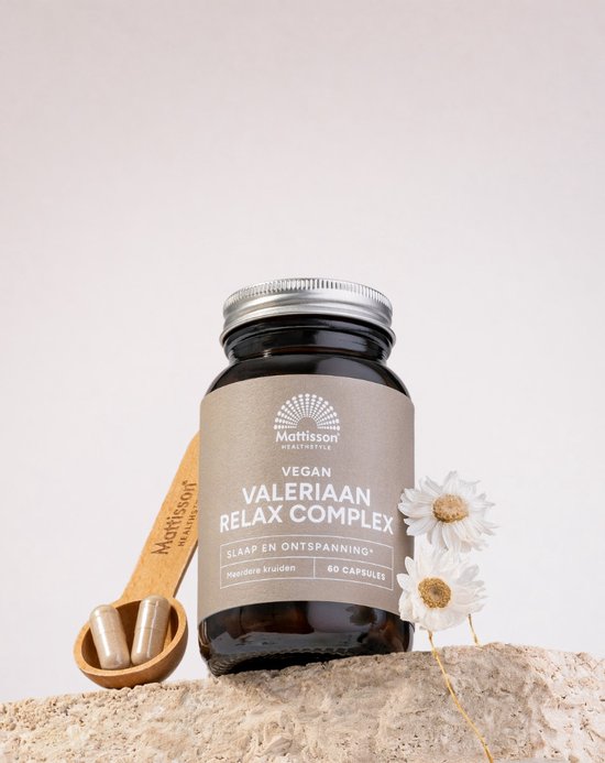 Bruine glazen pot met lichtbruin label, Mattisson HEALTHSTYLE VEGAN VALERIAAN RELAX COMPLEX, 60 capsules, met een houten lepel met 2 capsules erop, en 2 gedroogde bloemen.
