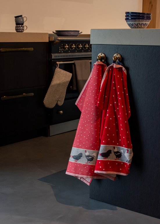 Deux torchons rouges à pois blancs avec une bordure de poules sont suspendus à un meuble de cuisine.