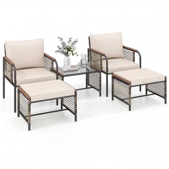 Een set van twee fauteuils met beige kussens, voetenbankjes en een salontafel met glazen blad. De meubels hebben een rotan afwerking.