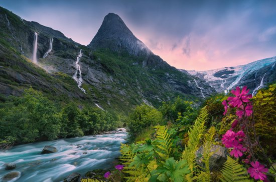 Turquoise rivier stroomt langs steile, groene berghellingen met watervallen, gletsjer en roze bloemen.