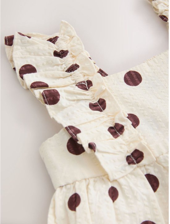 Crèmekleurige playsuit met bruine stippen en ruches aan de schouders.