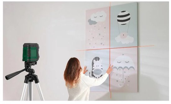 Vrouw hangt vier afbeeldingen op met behulp van een laserwaterpas op statief. Afbeeldingen met teddybeer, zebra, luchtballon en paraplu.