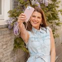 Femme joyeuse avec un étui de téléphone rose pâle avec cordon. Elle tient son téléphone en l'air.