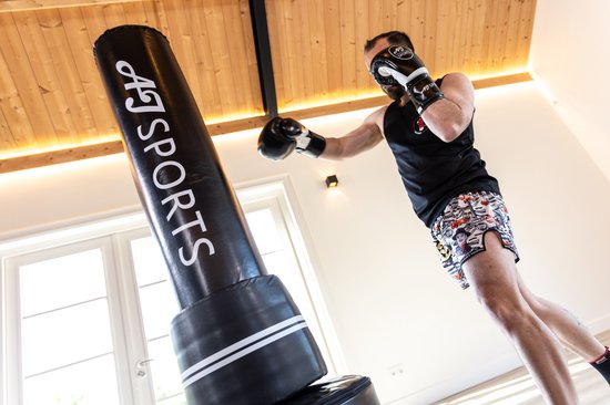 Man met bokshandschoenen slaat tegen zwarte AJ-Sports bokspaal.