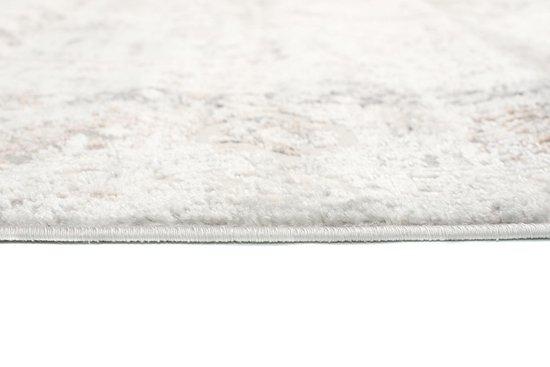 Détail du bord d'un tapis beige avec un motif subtil et délavé sur fond blanc.