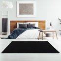 Tapis shaggy noir à poils longs devant un lit double avec une tête de lit en bois.