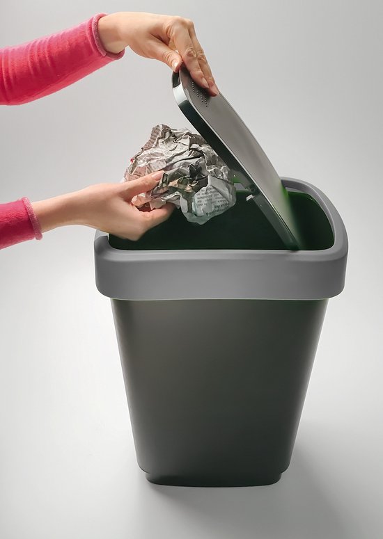 Hand met roze mouw gooit gekreukeld papier weg in een donkergrijze afvalbak met een grijze dekselrand.