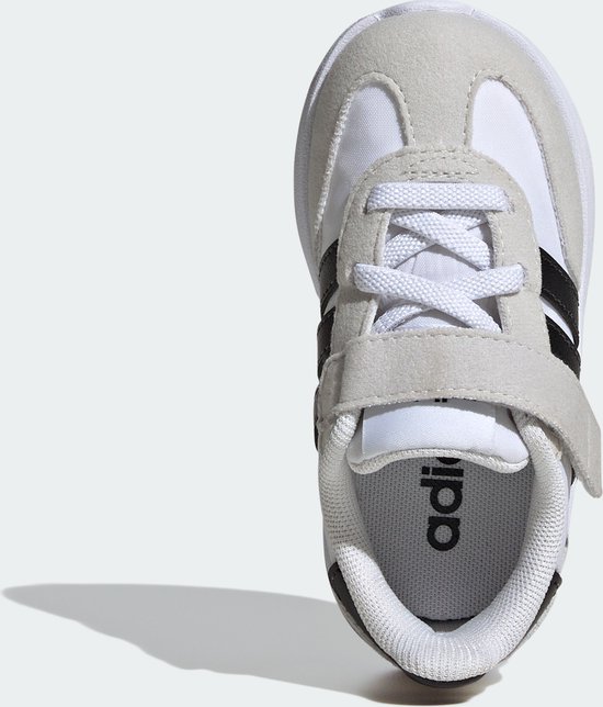 Vooraanzicht van een witte kindersneaker met zwarte Adidas-strepen, klittenbandsluiting en het Adidas-logo op de binnenzool.