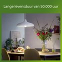 Een eettafel met een moderne witte hanglamp en een vaas met bloemen.